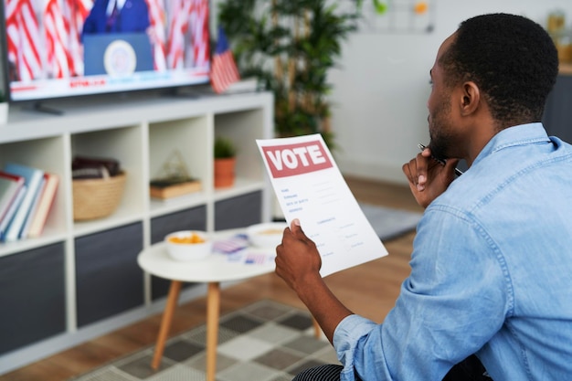 Schwarzer Mann sieht Fernsehen und hält ein Wahldokument in der Hand