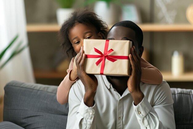 schwarzer Mann sitzt mit seiner Tochter auf der Couch, überraschende Geschenkkiste für den Vatertag