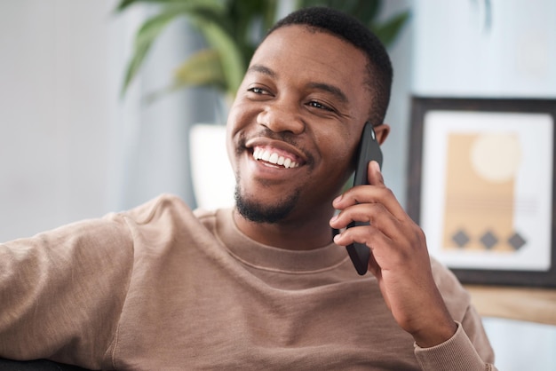 Schwarzer Mann telefoniert und entspannt sich im Haus und im Wohnzimmer mobile Kommunikation und Kontakt mit dem sozialen Netzwerk Fröhlicher junger Afrikaner, der über Smartphone-Gespräche und Handy-Technologie spricht