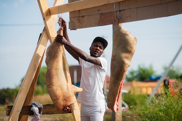 Schwarzer Metzger hängen Schweineschlachtkörper für die spätere Verarbeitung im Freien auf dem Land