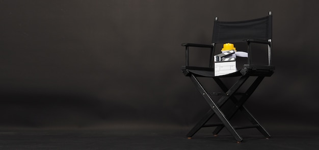 SCHWARZER Regiestuhl mit Clapperboard oder Film Clapper Board und Megaphon auf schwarzem Hintergrund. Verwendung in der Videoproduktion oder Film- und Kinoindustrie.