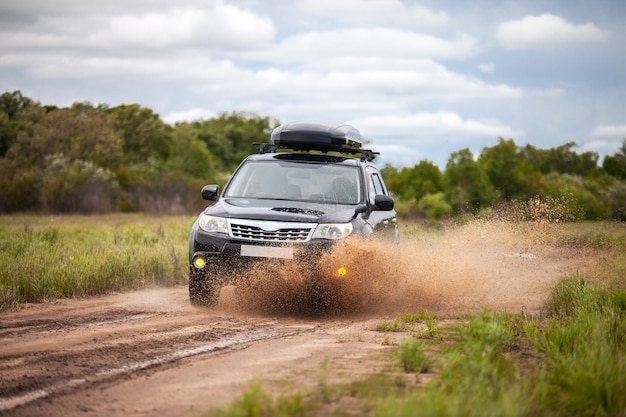 Schwarzer Subaru Forester bewegt sich auf einer schmutzigen Forststraße und macht viel Wasserspritzer