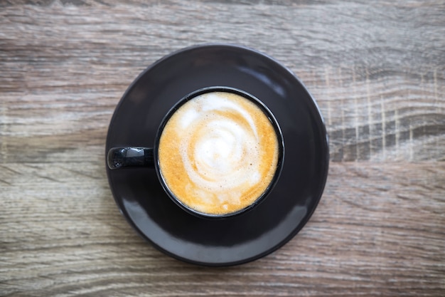 Schwarzer Tasse Kaffee mit dem Milchschaum, der auf altem Holztisch so köstlich ist