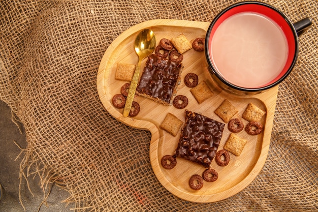 Schwarzer Tasse Kaffee mit Milch oder mit Kakao auf einem hölzernen Behälter in Form eines Herzens mit Schokoladenwaffeln