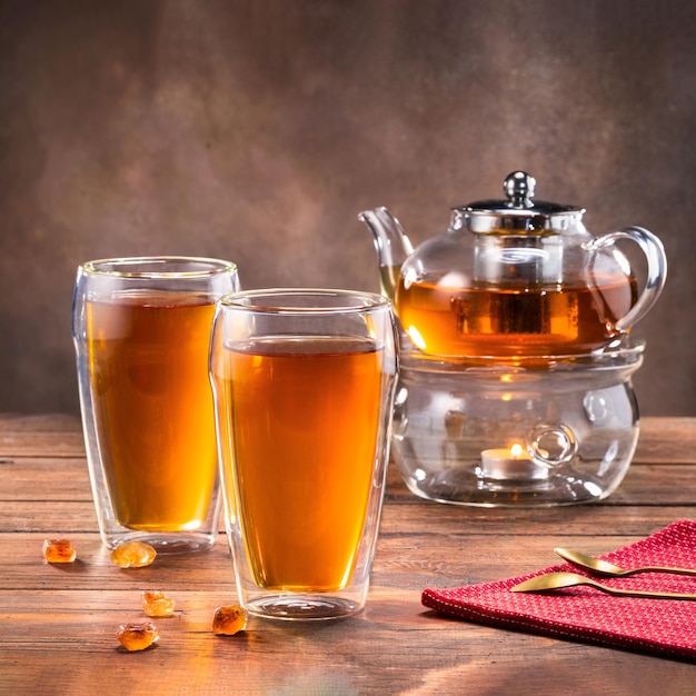 Schwarzer Tee in einer Teekanne aus Glas und Tassen auf dunklem Hintergrund Tee-Konzept