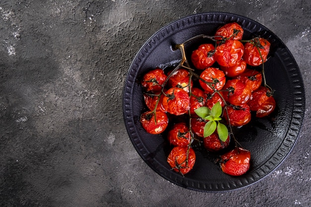 Schwarzer Teller mit Confit-Tomaten auf dunkler Oberfläche.