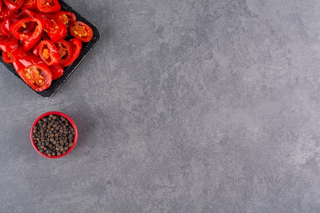 Schwarzer Teller mit geschnittenen roten Tomaten und Pfefferkörnern auf Steintisch.