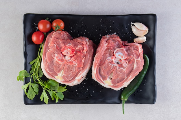 Schwarzer Teller mit rohem Lammfleisch auf Steintisch.