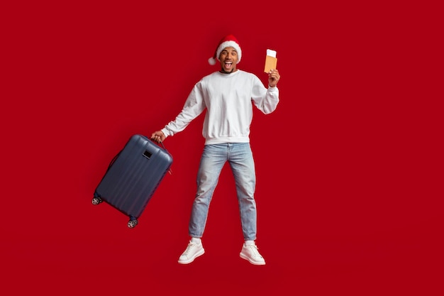 Schwarzer Tourist in Weihnachtsmütze, der über roten Hintergrund springt