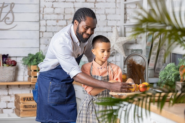 Schwarzer vater und sein sohnkind kochen frisches gemüse in der küche zu hause afrikanischer vater und junge kind p