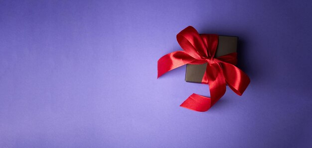 Schwarzes Geschenk mit rotem Band auf violettem Hintergrund Valentinstag Geburtstag oder Feiertage Konzept Platz kopieren