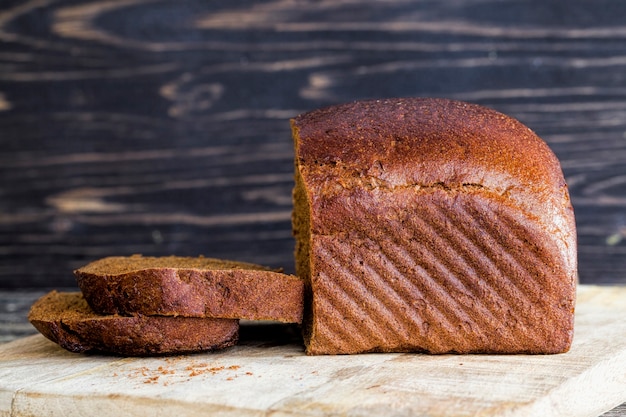 Schwarzes hausgemachtes Roggenmehlbrot, Nahaufnahme des Essens auf Küchenschneidebrett, kochendes Mittagessen