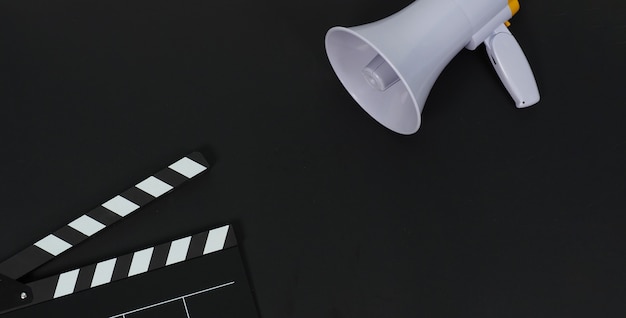 Schwarzes Klappbrett oder Filmklappe oder Schiefer und Magaphone auf schwarzem Hintergrund. Es wird in der Videoproduktion und Filmindustrie verwendet.