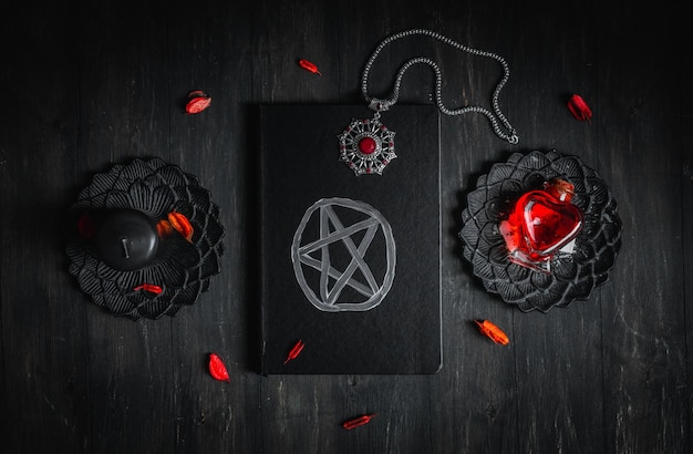 Schwarzes Lederbuch mit einem magischen Zeichen, einem Amulett, einer Kerze und einem roten Trank auf schwarzem Hintergrund