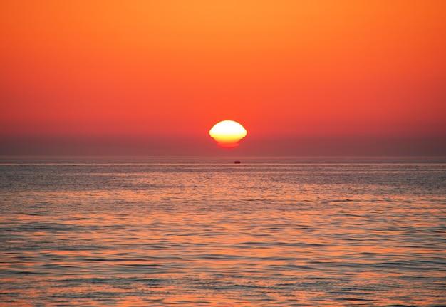 Schwarzes Meer bei Sonnenuntergang. Große gelbe Sonne unter der Meeresoberfläche. Sotschi, Russland.