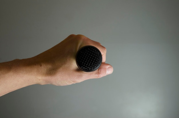 schwarzes Mikrofon in der Hand von vorne isoliert auf grauem Hintergrund