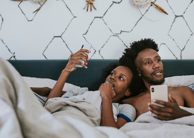 Schwarzes Paar im Bett mit einem Smartphone