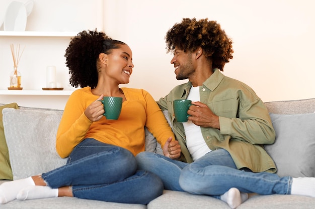 Schwarzes Paar umarmt sich, während es drinnen auf dem Sofa heißen Kaffee genießt