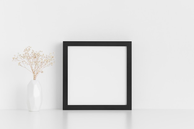 Schwarzes quadratisches Rahmenmodell mit einem Gypsophila in einer Vase auf einem weißen Tisch