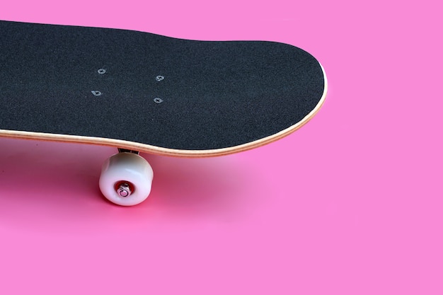 Schwarzes Skateboard auf rosa Hintergrund.