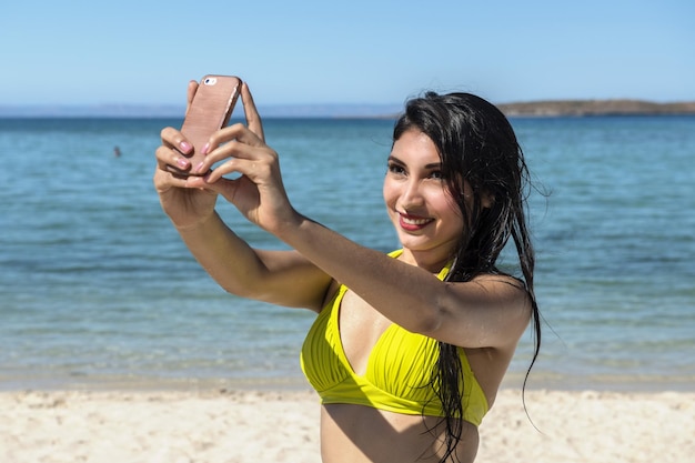 Schwarzhaariges Latina-Mädchenporträt, das Selfie auf dem Meereshintergrund macht