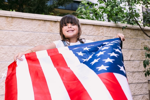 Schwarzhaariges Mädchen, das im Garten ihres Hauses eine Flagge der Vereinigten Staaten hält und schwenkt Konzept der Feier zum Unabhängigkeitstag Vereinigte Staaten von Amerika 4. Juli Patriotismus und amerikanischer Stolz