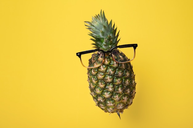 Schwebende Ananas mit Brille auf gelbem Hintergrund mit Kopierraum