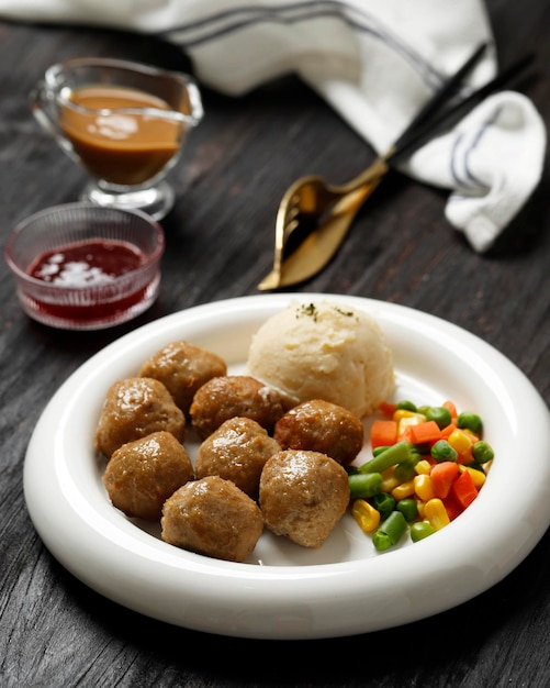 Schwedische Fleischbällchen mit cremiger Soße, Butterkartoffelpüree und Preiselbeersoße auf weißem Plattenholzhintergrund