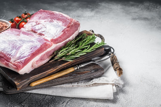 Schweinebauchblock rohes Fleisch mit Haut auf einem Holzbrett mit Rosmarin Weißer Hintergrund Draufsicht Kopierbereich