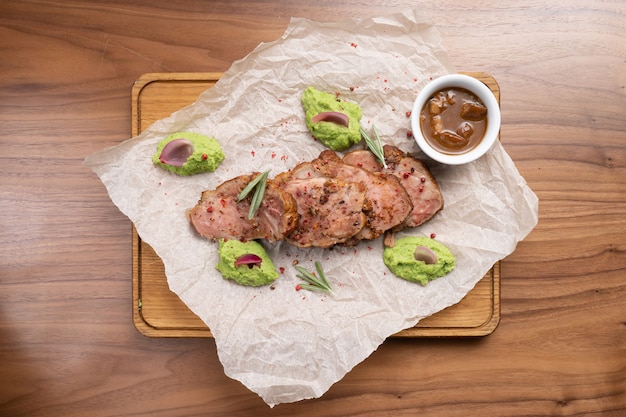 Schweinebratenstücke mit Gewürzen, Rosmarin, Erbsenpüree und Sauce auf einem Holztisch