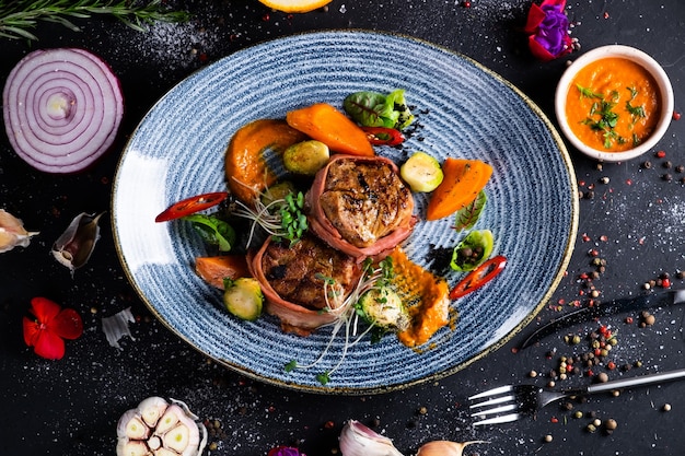 Schweinefiletmedaillons im Speck mit würziger Sauce und Rosenkohl auf dunkler Oberfläche