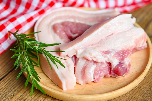 Schweinefleisch auf Holzteller mit Rosmarin frisches rohes durchwachsenes Schweinefleisch zum Kochen von Essen Schweinehaut Schweinehaut Draufsicht