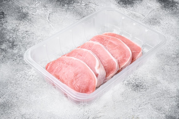 Schweinefleisch Frische Schweinesteaks in Plastikpackungsbehälter auf grauem Steintischhintergrund mit Kopierplatz für Text