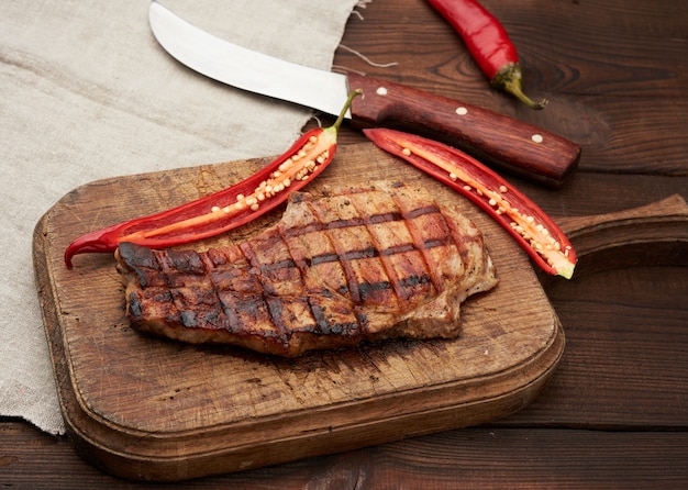 Schweinefleisch gebratenes Steak auf der Rippe liegt auf einem braunen Vintage-Holzbrett neben frischen roten Chilischoten