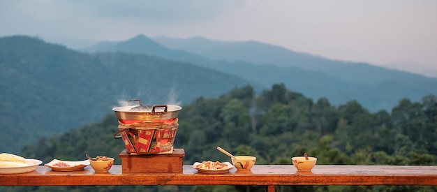 Schweinefleisch oder Fleisch mit Gemüse und Suppe auf der heißen Pfanne vor dem Hintergrund der Berge Der traditionelle thailändische Grillstil ist in Thailand berühmt