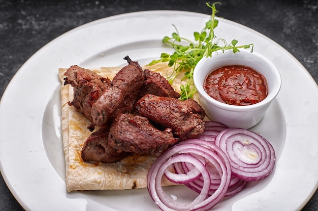 Schweinefleisch, Rindfleisch, Lammschaschlik mit Sauce, Zwiebeln und Lavash auf einem weißen Teller auf dunklem Hintergrund