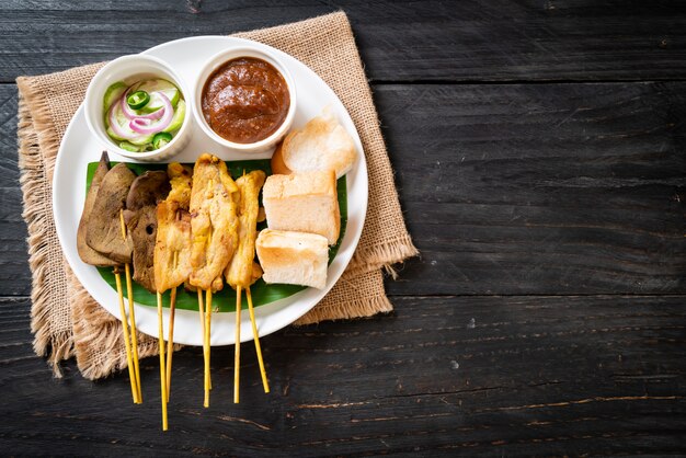 Schweinefleisch Satay mit Ihrer Erdnusssauce und Gurken, die Gurkenscheiben und Zwiebeln in Essig sind