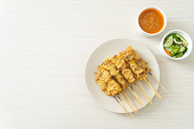 Schweinefleisch-Saté mit Erdnusssauce, Gurkenscheiben und Zwiebeln in Essig - asiatischer Essensstil