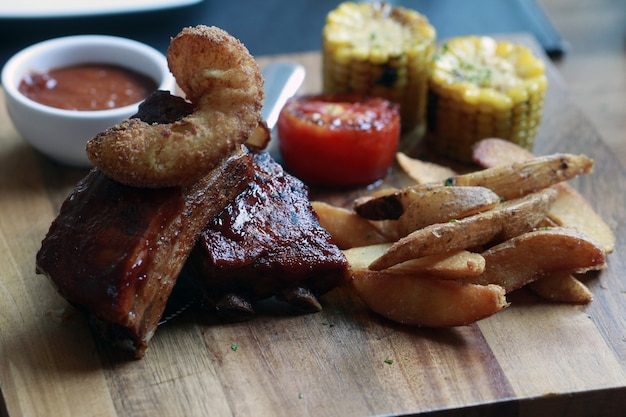 Schweinefleischrippe-Grillsteakaufschlag mit Pommes-Frites auf hölzerner Platte