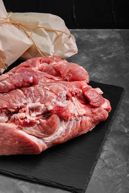 Schweinefleischschinken, frisches Fleisch auf einem Schieferteller auf grauem Hintergrund mit Gemüse.