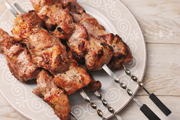 Schweinefleischspieße auf Spieße in einer Platte auf einem hölzernen Hintergrund