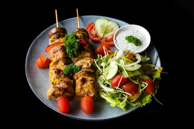 Schweinefleischspieße mit gegrilltem Gemüse, serviert mit Salat auf schwarzem Hintergrund, Seitenansicht