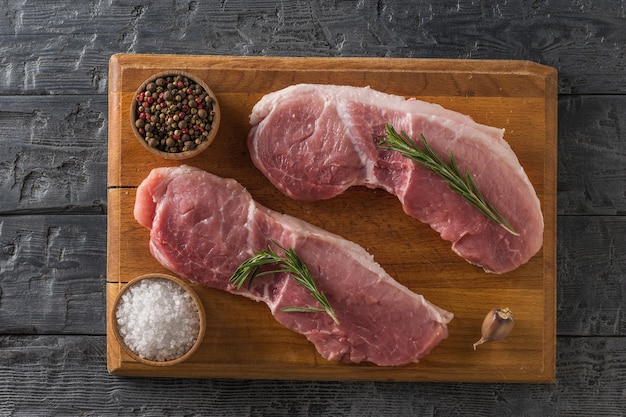 Schweinefleischstücke auf einem Schneidebrett mit Gewürzen auf einem rustikalen Tisch. Zutaten zum Kochen von Fleischgerichten.