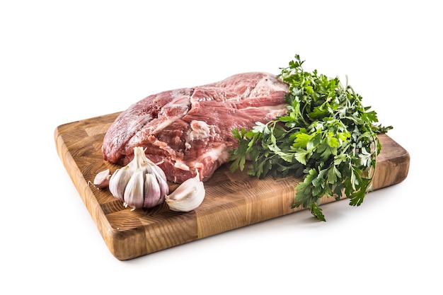 Schweinehals rohes Fleisch mit Knoblauch Petersilie Kräuter Tomaten und Rosmarin auf Metzgerbrett isoliert auf weißem Hintergrund.