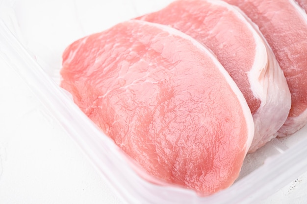 Schweinekotelett in Scheiben geschnittenes Frischfleisch-Set, im Plastikverpackungsbehälter, auf weißem Steintischhintergrund, mit Kopienraum für Text