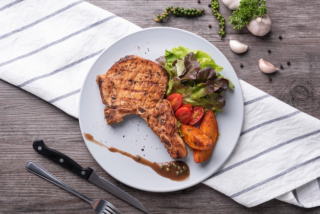 Schweinekotelettsteak mit Gemüsesalat und Kartoffelchips in weißer Platte. Draufsicht.