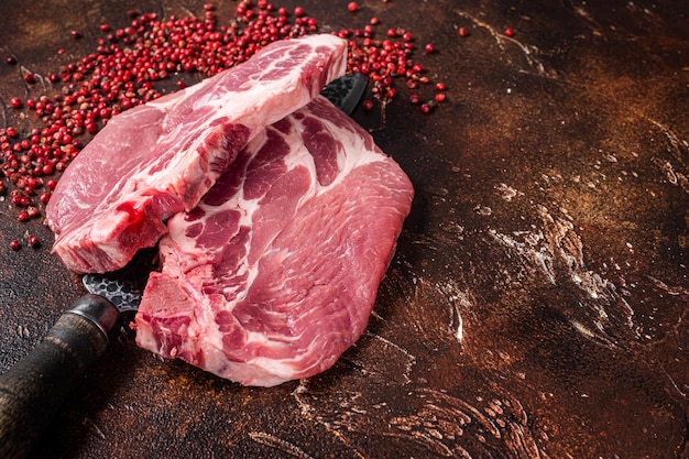 Schweinelendesteak aus rohem Nackenfiletfleisch auf Metzgermesser. Dunkler Hintergrund. Ansicht von oben. Platz kopieren.