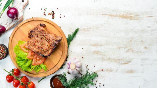 Schweinesteak am Knochen mit Gemüse auf dem Brett Grillmenü Draufsicht