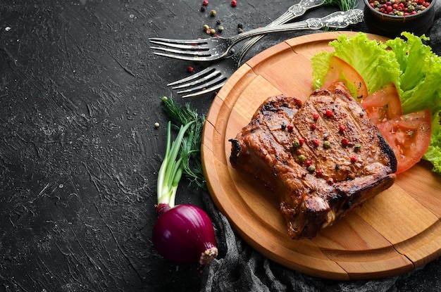 Schweinesteak am Knochen mit Gemüse auf dem Brett Grillmenü Draufsicht