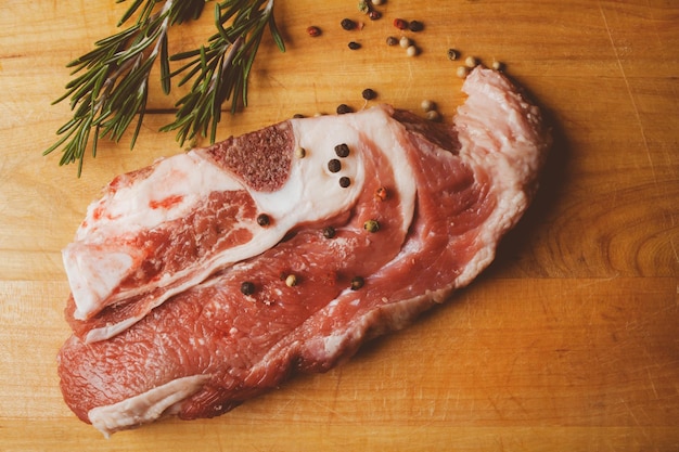 Schweinesteak mit Rosmarin und Pfeffer auf Holzhintergrund Rohes Fleischsteak Vintage-Fotoverarbeitung